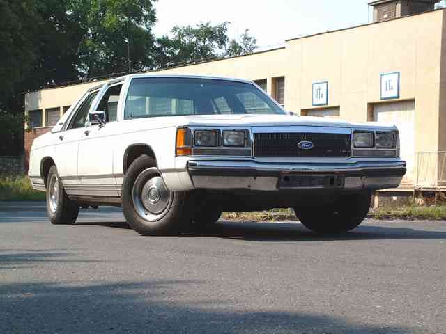 White Ford Crown Victoria sedan, front 3/4 view, parked outside a beige building