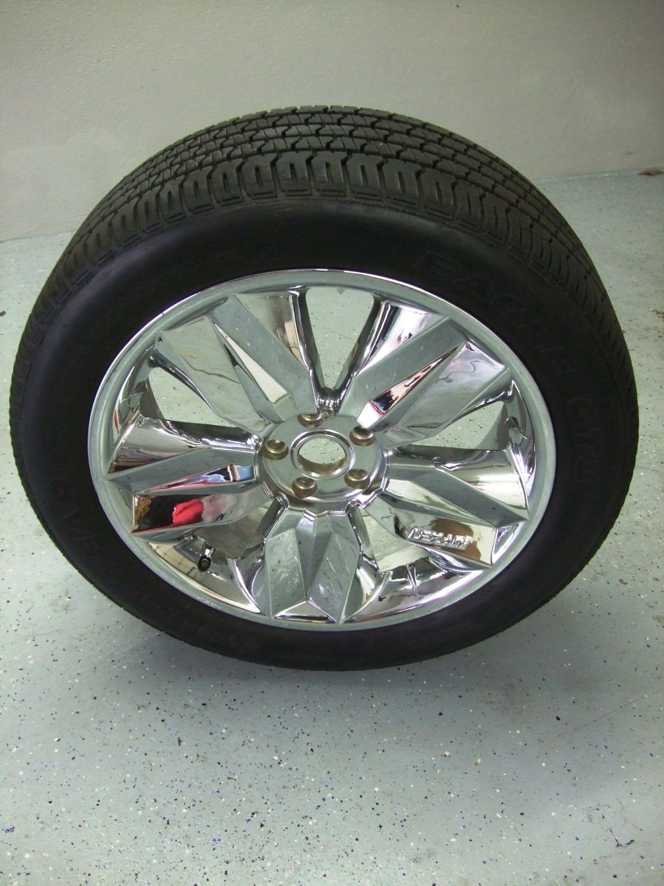Chrome wheel with a tire on it, sitting on a speckled floor