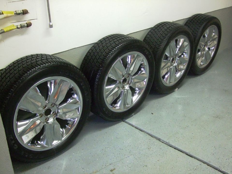 Four chrome wheels with tires lined up against a wall