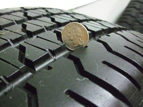 1987 Ford Bronco - Tire tread depth measured with a quarter coin. The coin is standing upright on the tread blocks.
