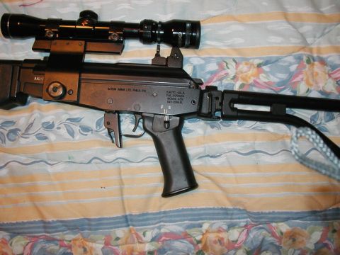 1993 Ford Bronco - Close-up view of an assault rifle equipped with a scope and a folding stock, resting on a patterned surface.
