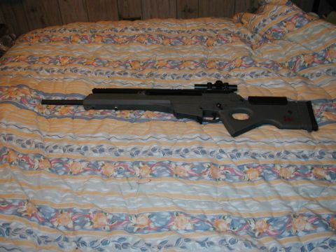 1993 Ford Bronco - A tactical rifle with a scope rests on a patterned bedspread, with wood paneling visible in the background.