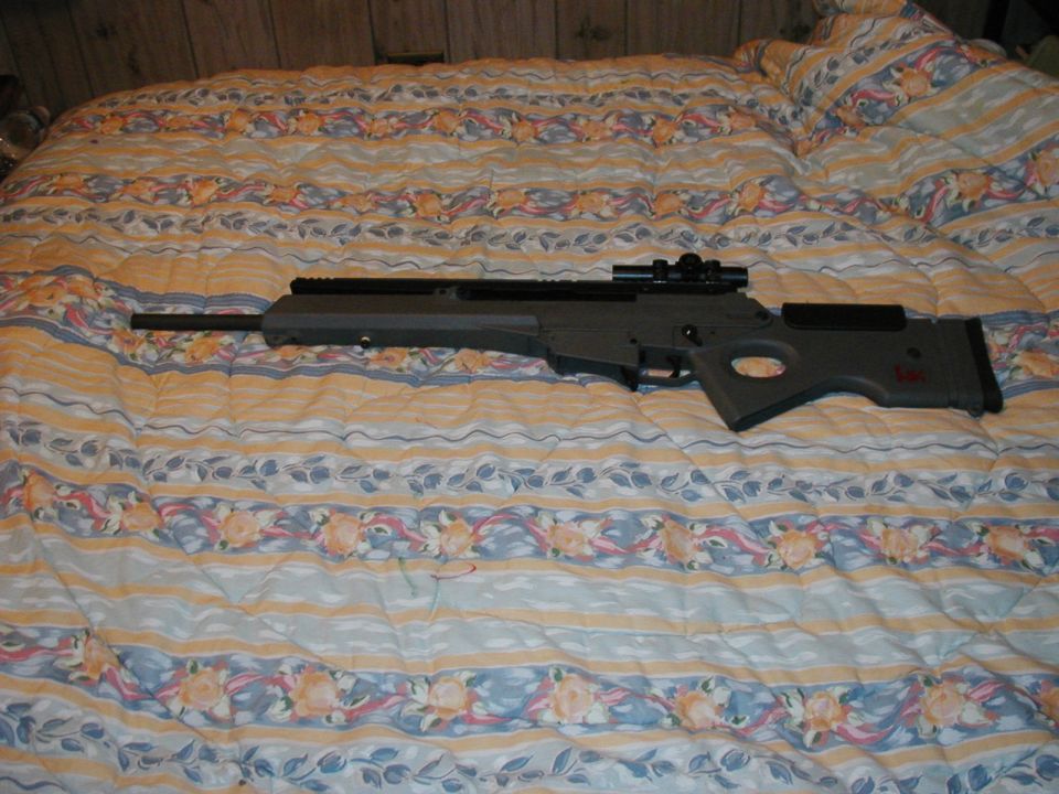 Sniper rifle with scope on a bed with a floral comforter