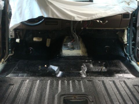 1996 Ford Bronco - The interior floor of a vehicle is exposed and coated, with wiring visible near the dashboard.
