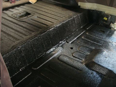 1996 Ford Bronco - The interior floor of a vehicle shows a black textured coating with raised ribs and a central opening.
