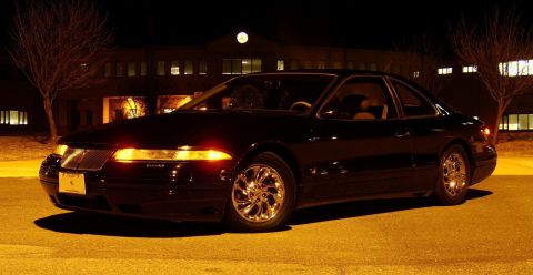 1996 Mercury Grand Marquis - A black coupe with chrome wheels is parked outside a building at night.