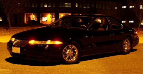 1996 Mercury Grand Marquis - A black coupe is parked outside a building at night with its headlights on.