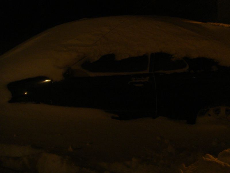 Side view of a dark-colored car covered in snow at night