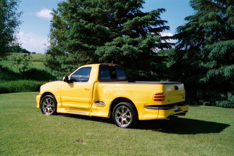 Yellow lowered Ford F-150 regular-cab pickup with chrome wheels on a lawn