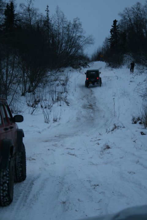 2003 Jeep TJ - Two Jeeps navigate a snow-covered incline in a wooded area.