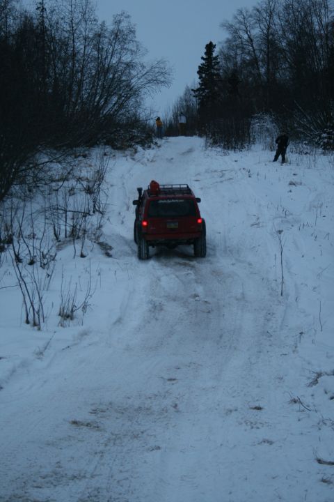 2003 Jeep TJ - A red 2003 Jeep TJ navigates a snow-covered incline, equipped with a roof rack for off-road adventures.