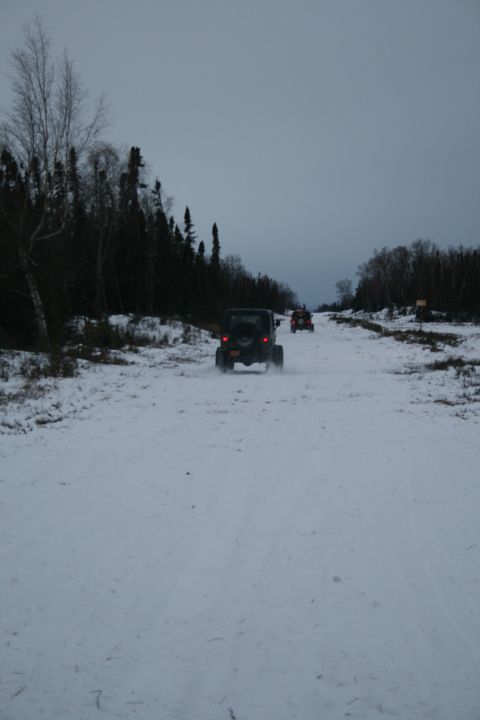 2003 Jeep TJ - Multiple off-road vehicles traverse a snowy trail surrounded by trees under an overcast sky.