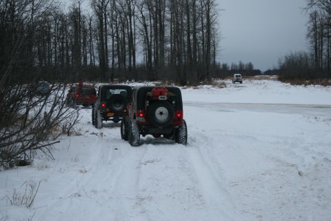 2003 Jeep TJ - A convoy of Jeeps navigates a snow-covered path through a wooded area under an overcast sky.