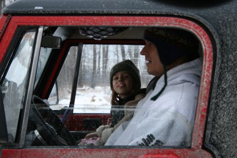 2003 Jeep TJ - A man and child sit inside a red Jeep, with snow visible on the exterior.