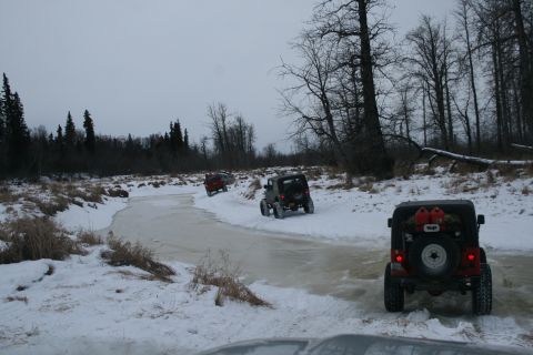 2003 Jeep TJ - Several Jeeps navigate a frozen, snow-covered riverbed surrounded by trees.