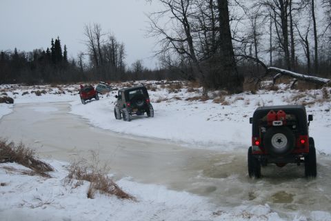 2003 Jeep TJ - Multiple Jeeps navigate a frozen, snow-covered path in a wooded area.
