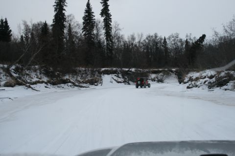 2003 Jeep TJ - A red off-road vehicle travels down a snow-covered path bordered by trees and snow-laden banks.