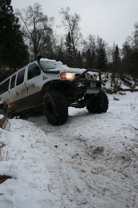 2003 Jeep TJ - A heavily modified van navigates a snowy terrain with its large tires and snorkel visible.