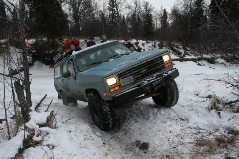 2003 Jeep TJ - A blue Chevrolet Suburban navigates a snowy path with trees in the background.