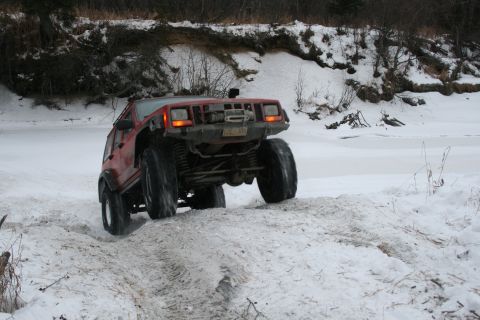 2003 Jeep TJ - A red Jeep Cherokee XJ navigates a snowy path near a frozen body of water.