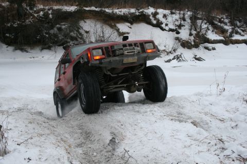 2003 Jeep TJ - A red Jeep Cherokee XJ navigates a snowy trail with its suspension clearly visible.