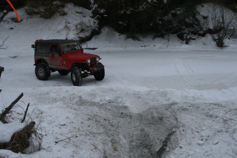 2003 Jeep TJ - A red Jeep Wrangler is parked on a snowy bank next to a frozen river.