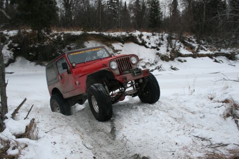 2003 Jeep TJ - A red Jeep Wrangler navigates a snowy, icy terrain near a frozen river, with 'KODIAK OFF-ROAD' visible on its windshield.