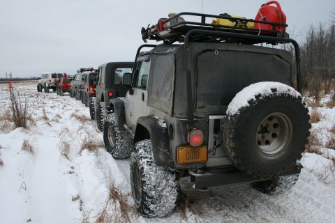 2003 Jeep TJ - A convoy of Jeeps navigates a snowy trail, with the lead vehicle showing its rear and spare tire.