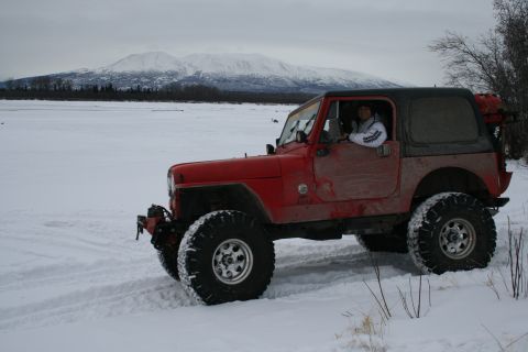 2003 Jeep TJ - A red Jeep Wrangler navigates a snowy landscape with snow-capped mountains visible in the distance.