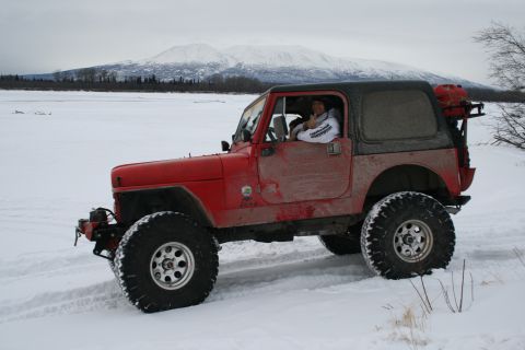 2003 Jeep TJ - A red 2003 Jeep TJ navigates a snowy landscape with mountains in the distance.
