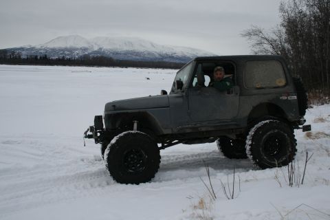 2003 Jeep TJ - A gray Jeep Wrangler navigates a snowy landscape with snow-capped mountains in the distance.