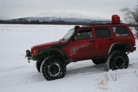 2003 Jeep TJ - A red Jeep Cherokee XJ is driven through a snowy landscape with mountains in the distance.