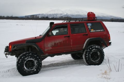 2003 Jeep TJ - A red Jeep Cherokee XJ navigates a snowy landscape with a jerrycan on its roof rack.