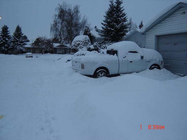 White pickup truck buried in snow next to a garage