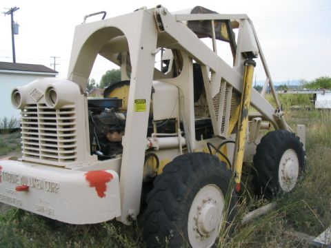 1979 Ford F-150 - An old industrial loader sits in a grassy field, its engine exposed and front bumper showing signs of wear.