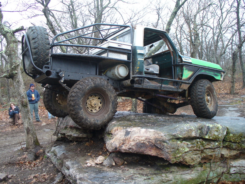 Modified green and white truck with roll cage on rocks