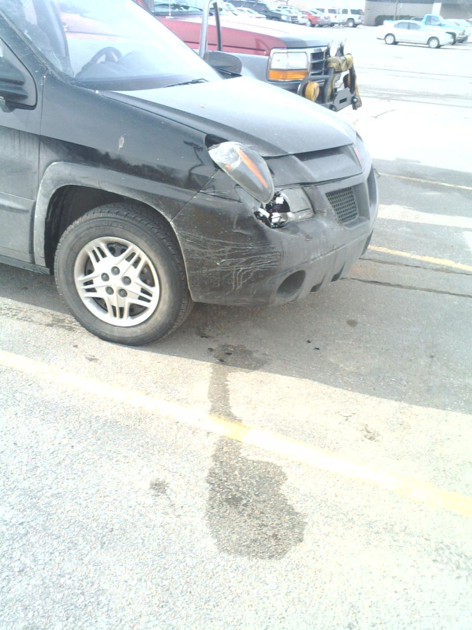Black Pontiac Aztek with damaged, hanging headlight and scraped front bumper in a parking lot