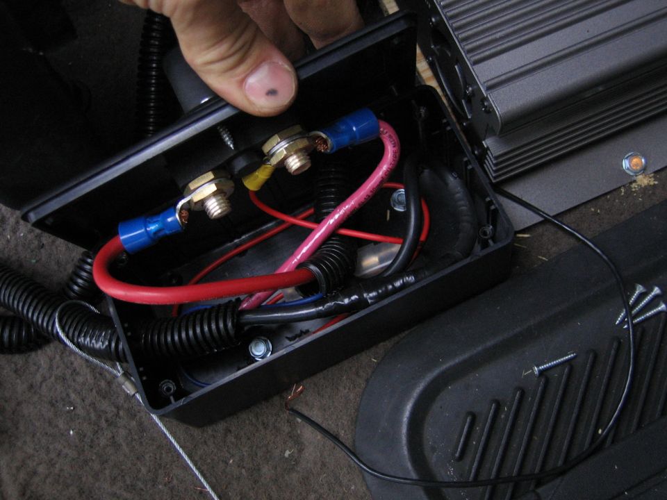 Open car audio distribution block with red power cables and gold studs beside an amplifier