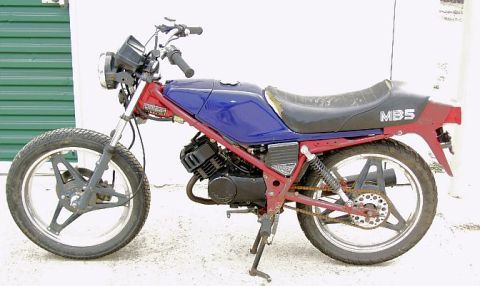 1985 Ford Crown Victoria LTD - A red and blue motorcycle with a black seat and 'MB5' marking is parked outdoors.