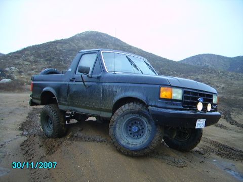 1990 Ford Bronco - 1990 Ford Bronco navigates a muddy trail with off-road tires.