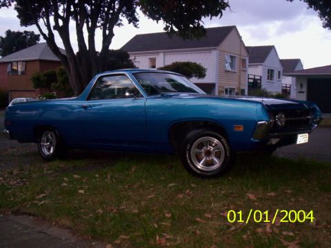 1970 Ford Ranchero - A blue 1970 Ford Ranchero is seen from a three-quarter front view, parked on a grassy area in front of houses.