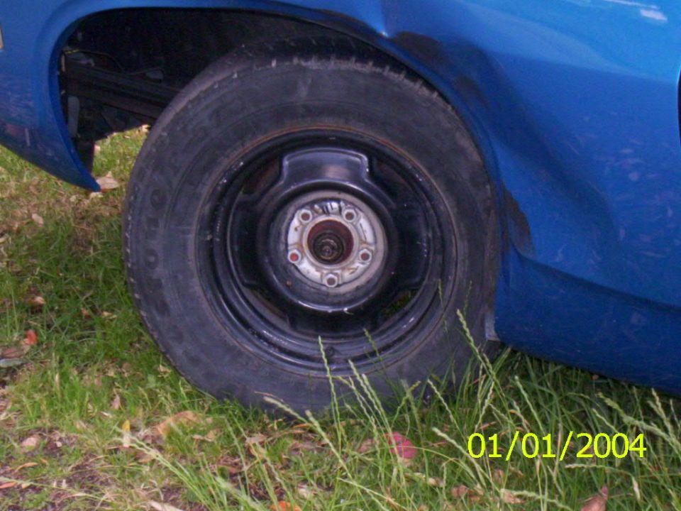 Close-up of a blue car's rear wheel and fender. Date stamp reads 01/01/2004