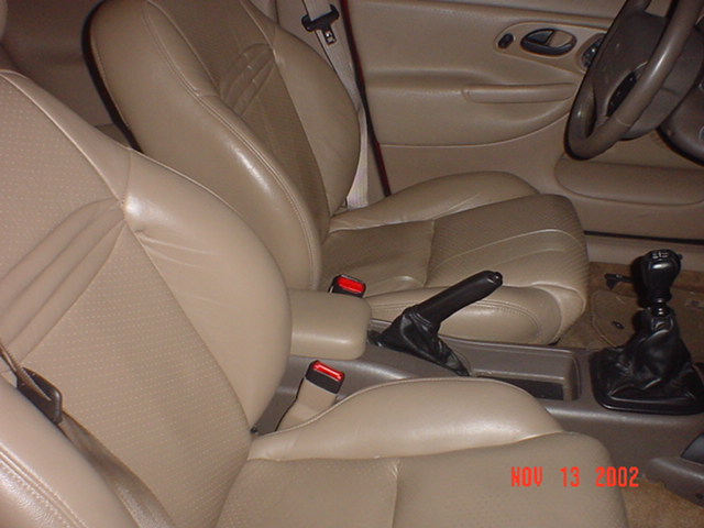 Tan leather front bucket seats with manual shifter and handbrake in a sedan interior