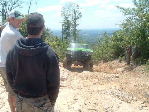 1978 Ford Bronco - A lifted green 1978 Ford Bronco navigates a steep, rocky incline on an off-road trail with spectators watching.