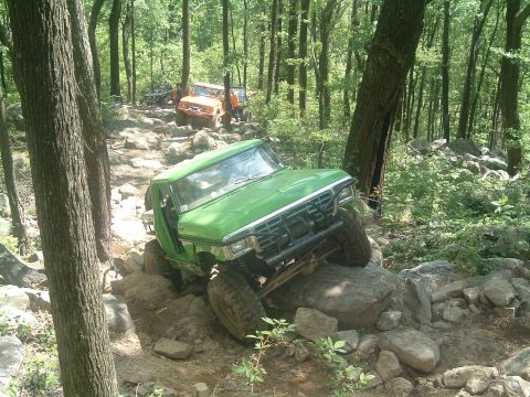 1978 Ford Bronco - A 1978 Ford Bronco navigates a challenging rocky trail in a forest setting, with another vehicle behind it.