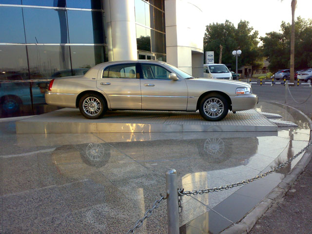 Gold Lincoln Town Car parked on a raised platform in front of a modern building