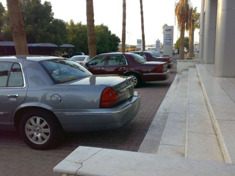 1999 Mercury Grand Marquis - Two Ford Crown Victorias are parked in front of a building with palm trees.