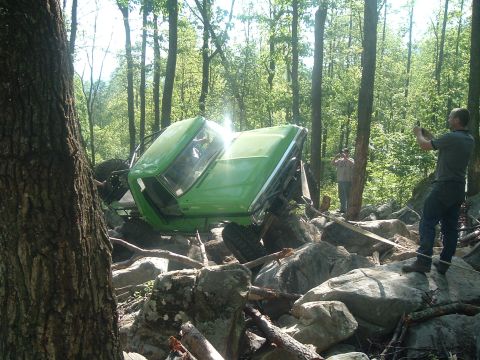 1978 Ford Bronco - A green off-road vehicle is stuck on a rocky trail with two onlookers documenting the situation.