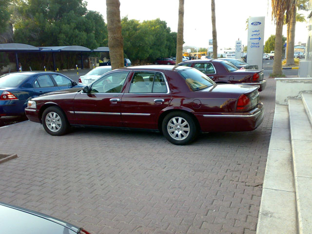 Maroon sedan parked on brick pavement, side view. Another similar car is behind it
