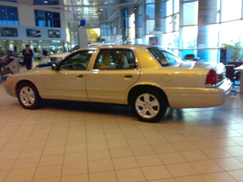 1999 Mercury Grand Marquis - Gold 1999 Mercury Grand Marquis displayed in a dealership showroom with tiled flooring.